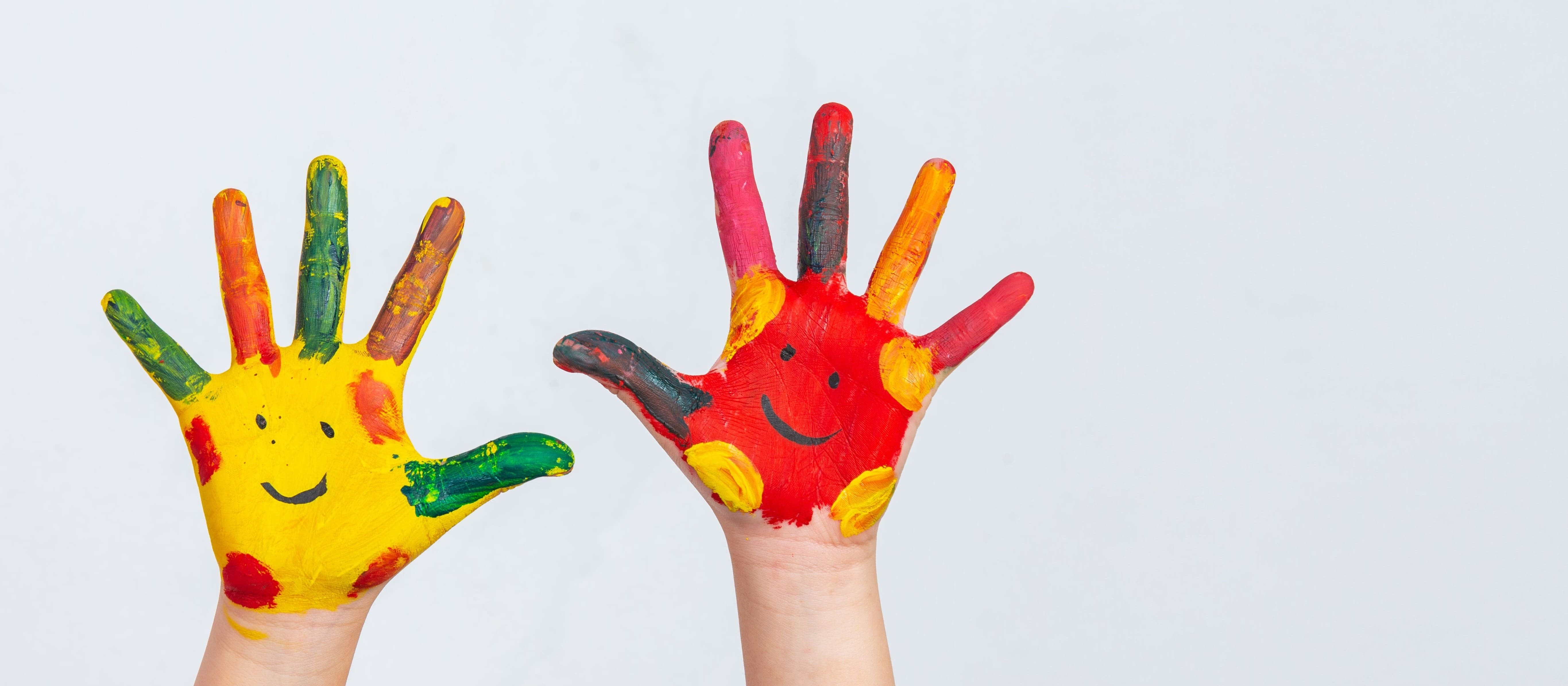 Mãos de uma criança com os dedos sujos de tinta colorida.
